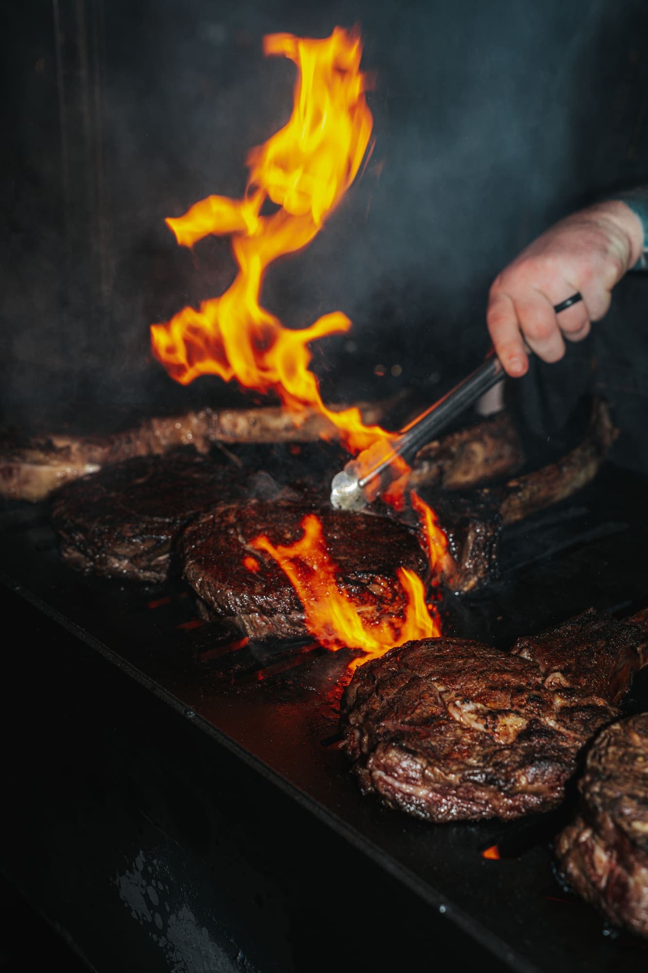 Steaks over open flame, turned with tongs